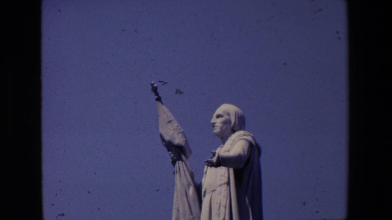 Stone statue with flag seen from below against blue sky.