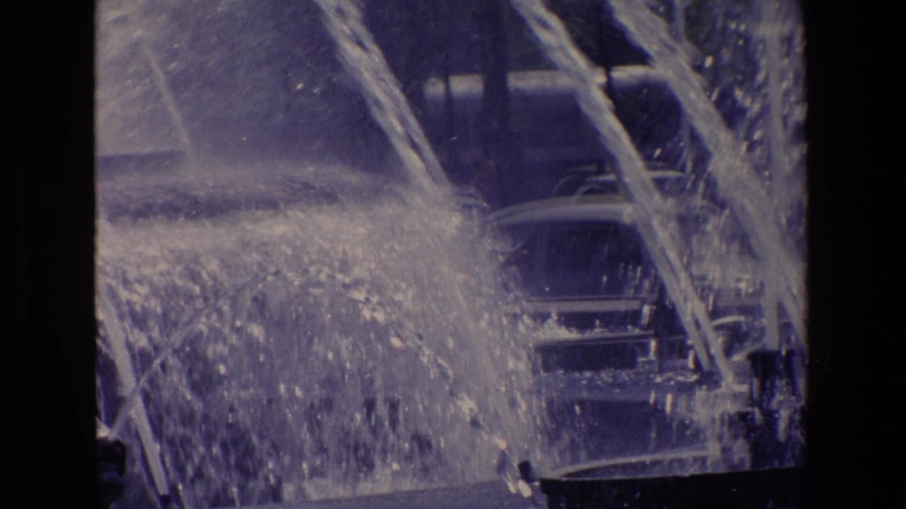Fountain spray crossing in front of cars on a city street.