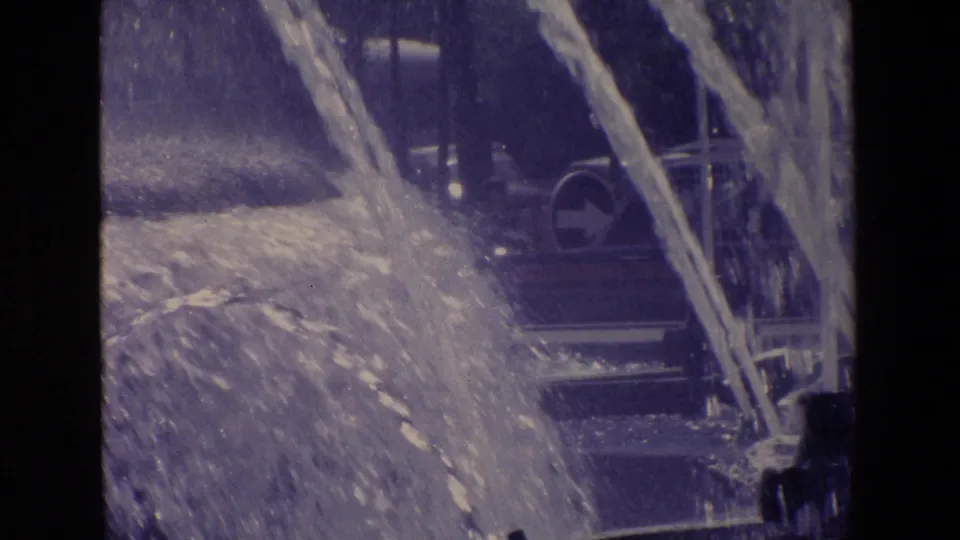 Fountain water fills the foreground while a bus or large street vehicle appears behind the spray in 1967 Madrid footage.