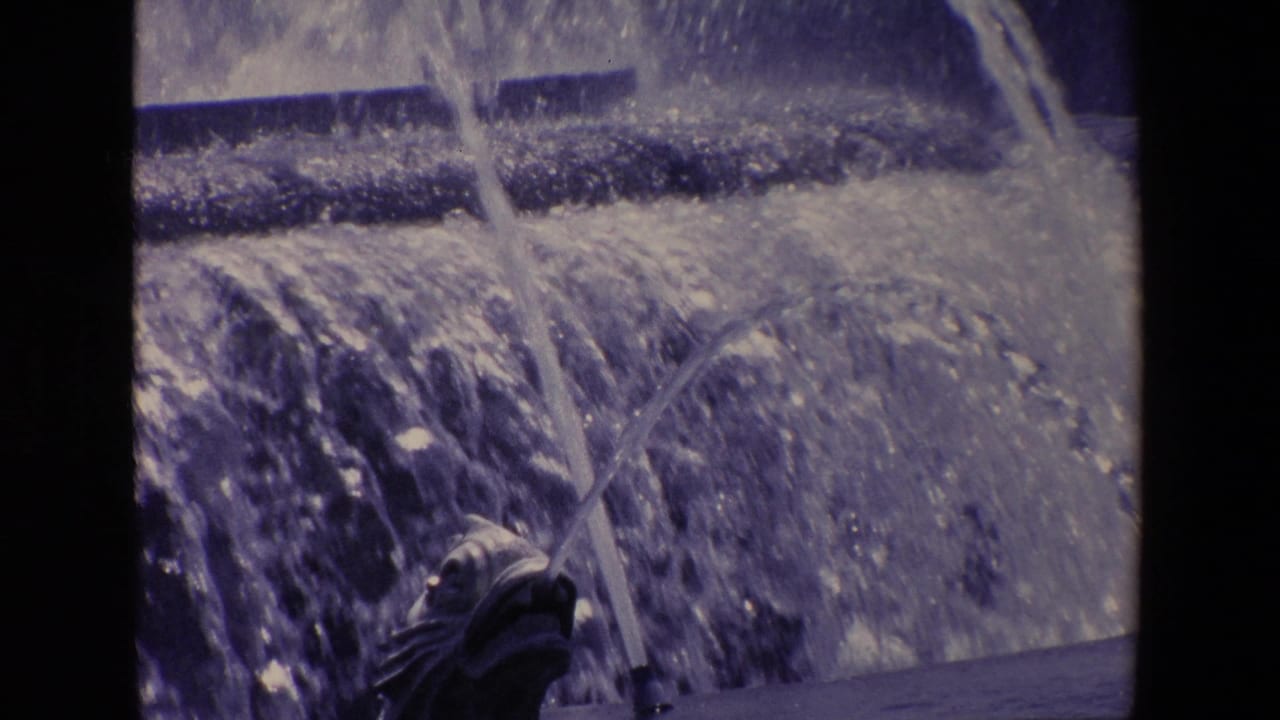 Close 1967 Madrid home-movie view of a fish-shaped fountain spout with water arcing and cascading over stone tiers.