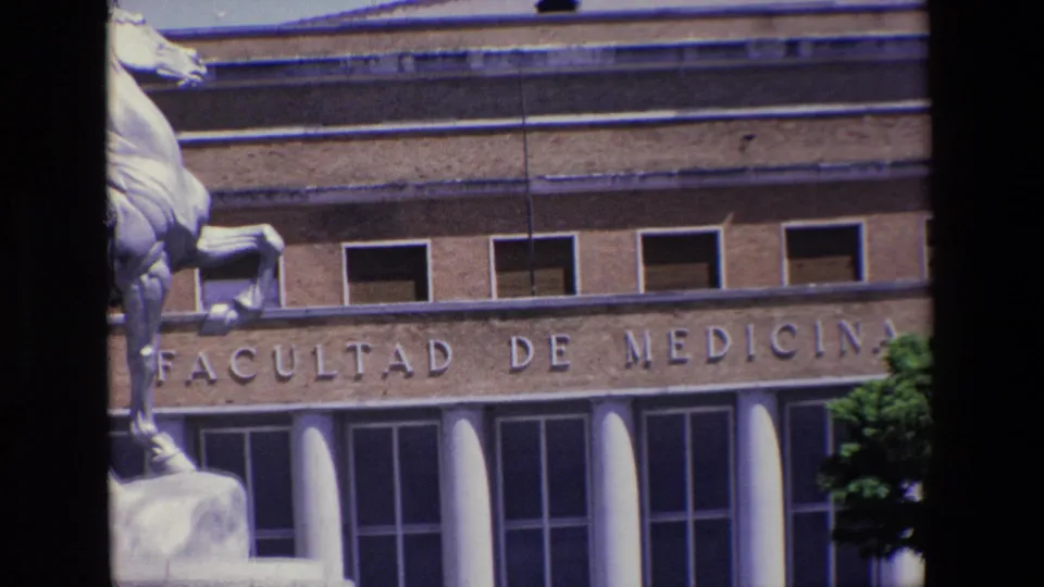 1967 Madrid frame of the Facultad de Medicina exterior, with the stone-lettered facade, rows of windows, white columns, and the left portion of an equestrian statue visible.