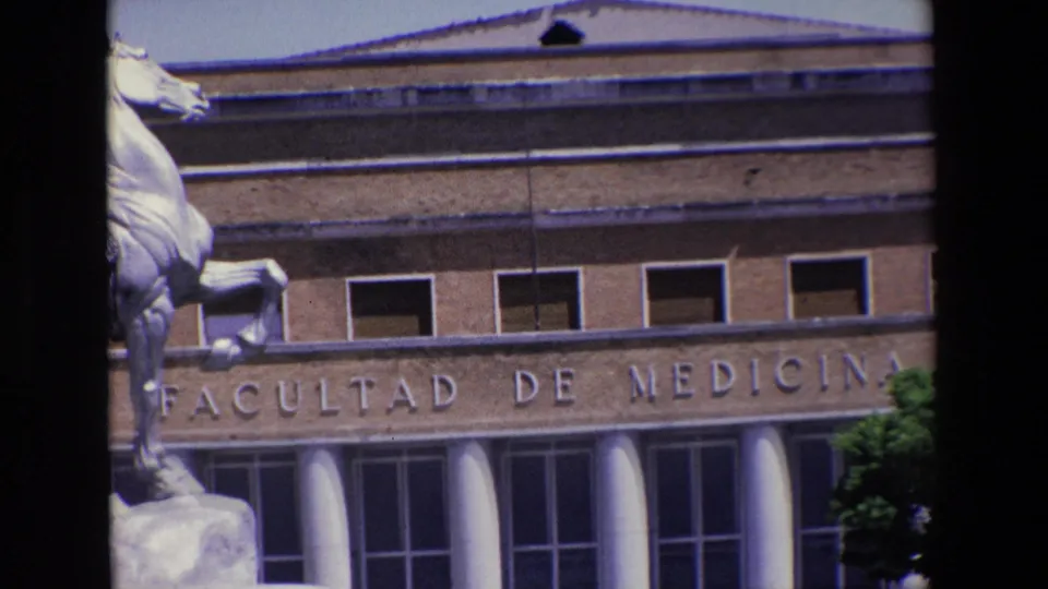Home-movie frame from Madrid in 1967 showing the Facultad de Medicina inscription, columned entrance area, upper windows, and the cropped equestrian statue along the left side.