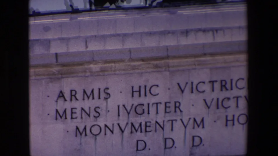 Tight 1967 Madrid home-movie close-up of the Victory Arch inscription, with large carved Latin lettering and pale stonework filling the frame.