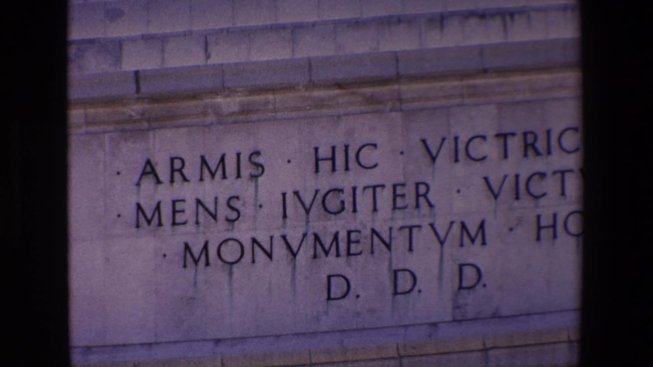 1967 Madrid home-movie frame showing a close-up of a stone monument inscription with Latin lettering, partially obscured by dark frame edges.