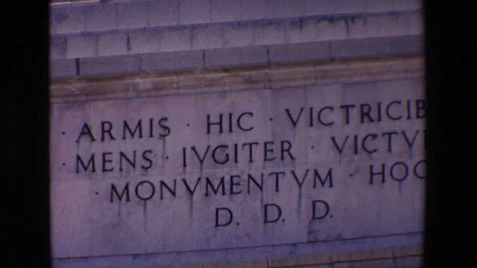 1967 Madrid home-movie frame with a cropped close-up of a stone inscription reading in part ARMIS, HIC, VICTRICIBUS, MENS, IVGITER, and MONVMENTVM.