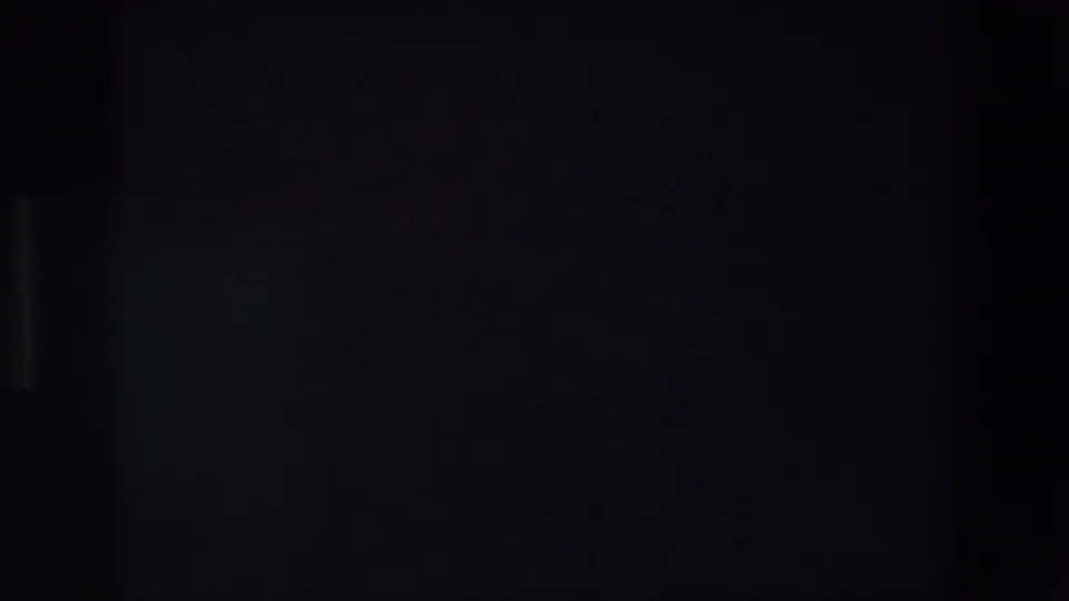 End frame from the Madrid 1967 home-movie clip, largely underexposed or blocked by shadow, with only a faint vertical band and minimal street detail visible.