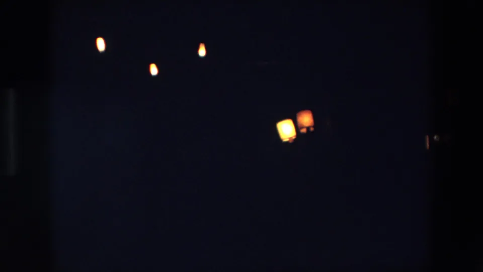 Palermo, Italy 1967 home-movie frame showing a very dark night sky with small glowing lantern-like lights softened by 8mm grain and low exposure.