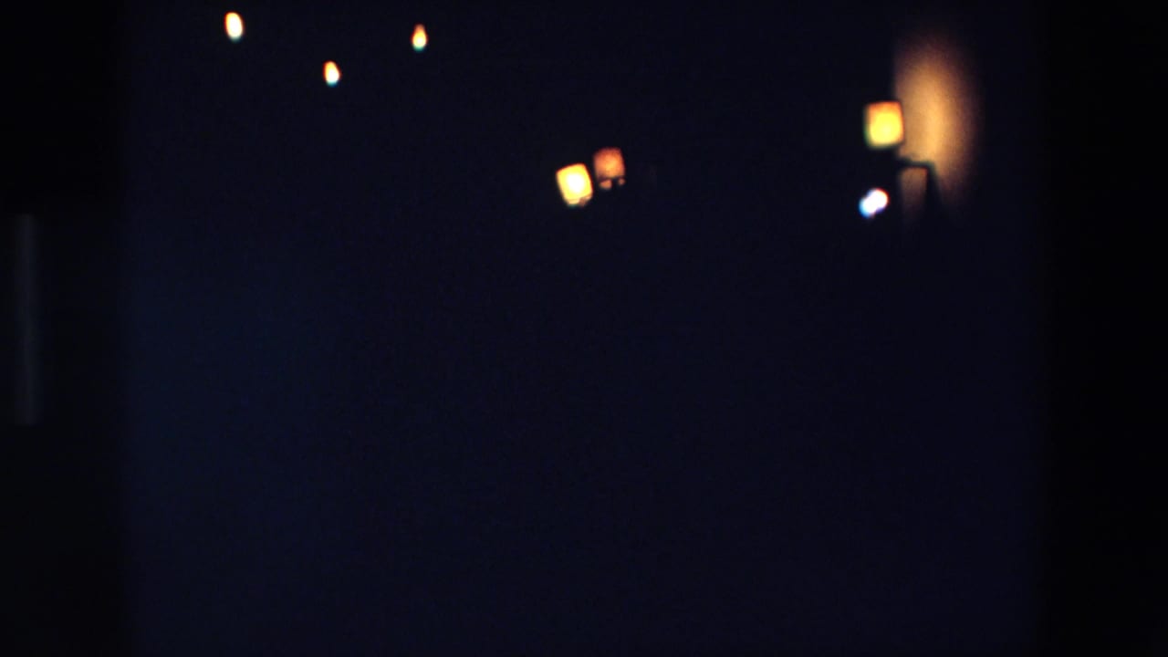 1967 Palermo home-movie frame showing scattered warm lights in deep darkness, with soft focus and visible 8mm grain.