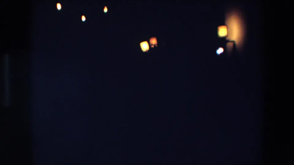 1967 Palermo home-movie frame showing scattered warm lights in deep darkness, with soft focus and visible 8mm grain.
