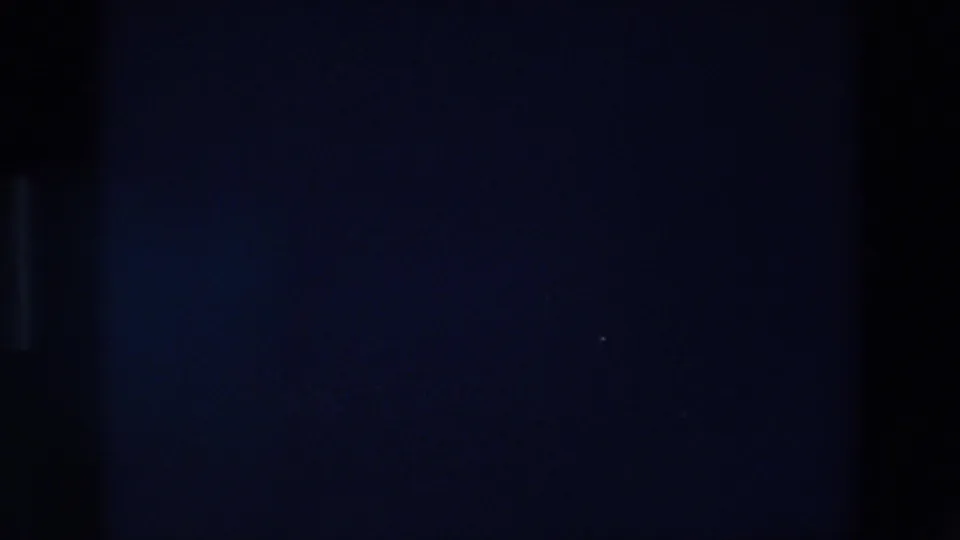 Low-light 8mm frame from the Palermo night sequence with faint vertical forms and little visible detail beyond the dark exposure.