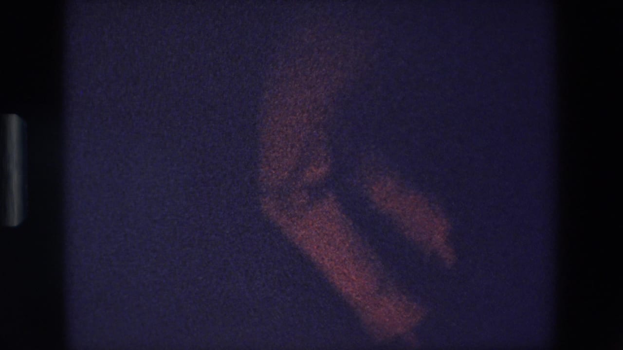 A heavily grainy 1967 Palermo 8mm frame appears to show a blurred dancer or performer moving in low light against a dark purple-blue background.