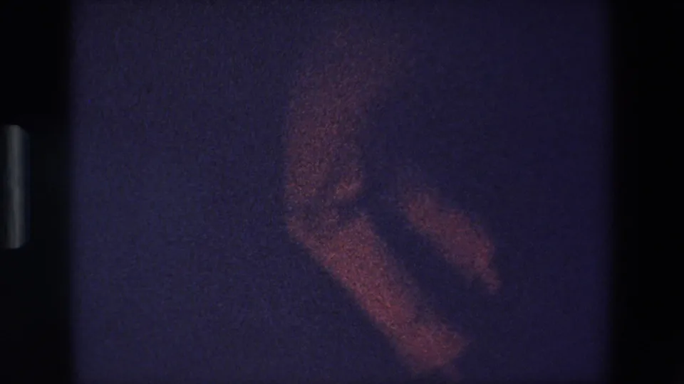 A heavily grainy 1967 Palermo 8mm frame appears to show a blurred dancer or performer moving in low light against a dark purple-blue background.