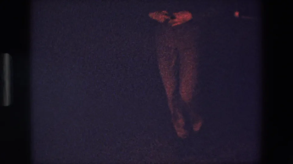 1967 Palermo 8mm frame showing a standing male dancer partially visible in low light, with his legs and hands catching reddish illumination against a dark background.