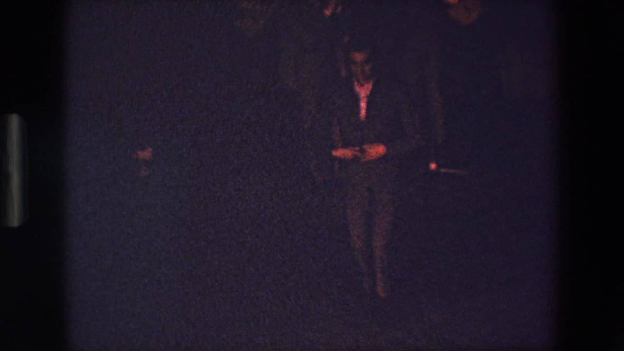 A dark-clad figure appears in a grainy, underexposed 1967 Palermo home-movie frame with reddish highlights and little visible background detail.