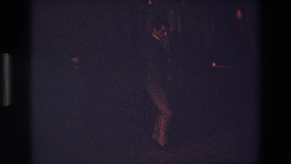 A partially visible person appears to lean or shift in a dark outdoor 1967 Palermo frame, with red-orange highlights and heavy 8mm grain obscuring detail.