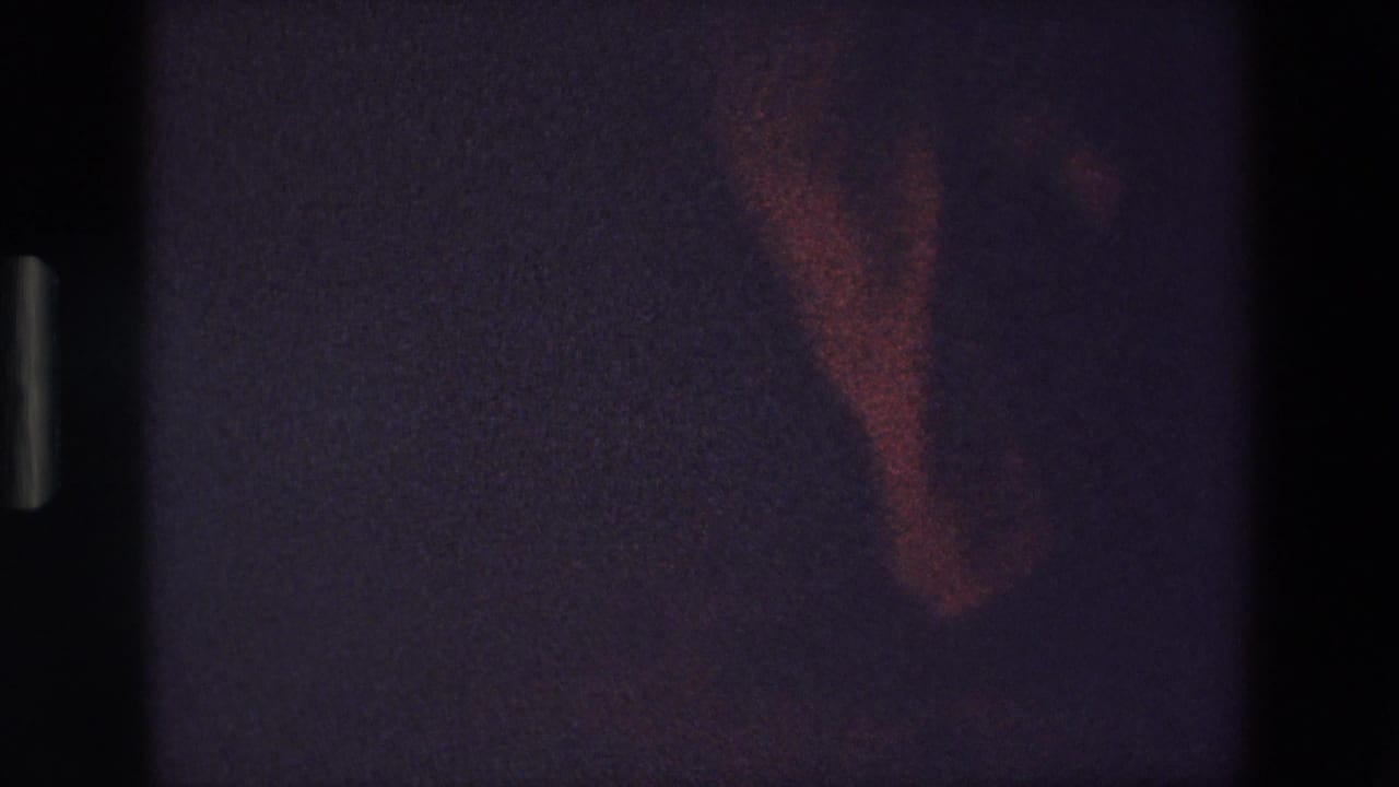 A shoe and trouser leg caught in reddish light against a dark interior.