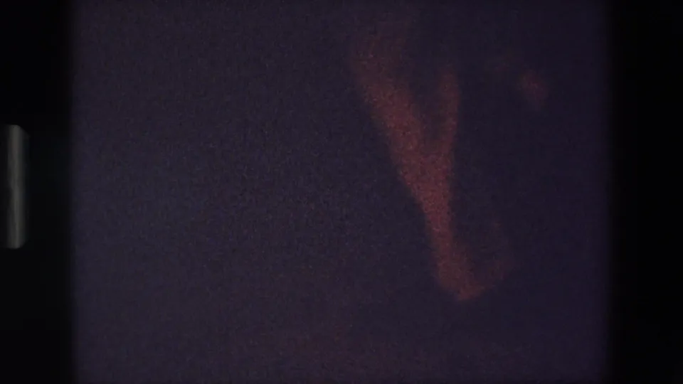 The frame shows a partial view of the dancer's foot and slacks in a dark Palermo interior, with grain and reddish exposure from the 8mm scan.