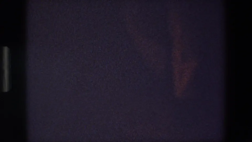 A faint lower-body silhouette appears near the floor in the underexposed 8mm frame, suggesting continued dance steps in the same dark room.