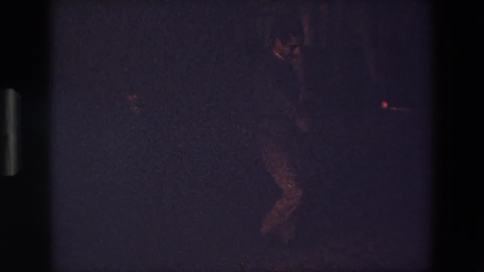 A dim 1967 Palermo home-movie frame shows a man in dark clothing dancing, with his lower body most visible against a grainy purple-black background.