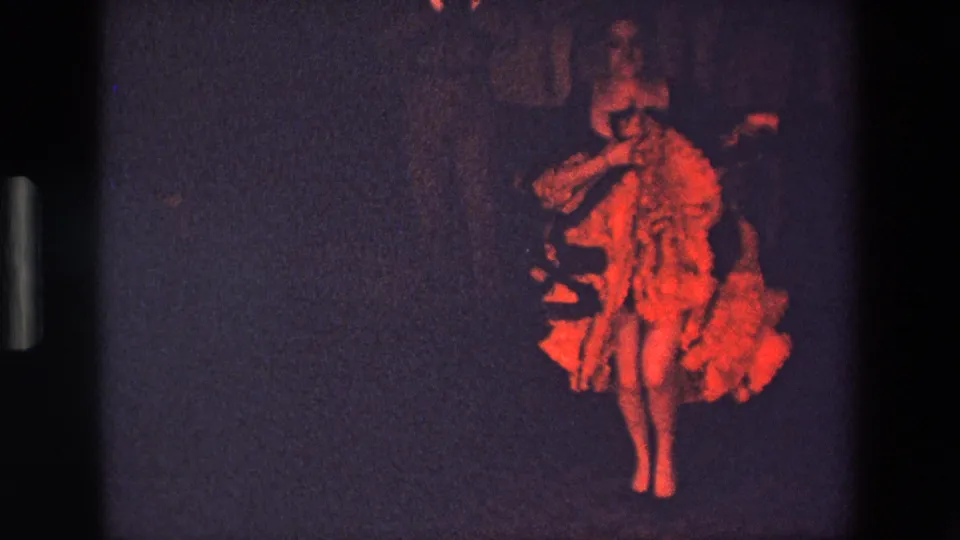 In this 1967 Palermo home-movie frame, a woman in a red ruffled costume appears mid-dance under dim stage lighting, with visible 8mm film edges.