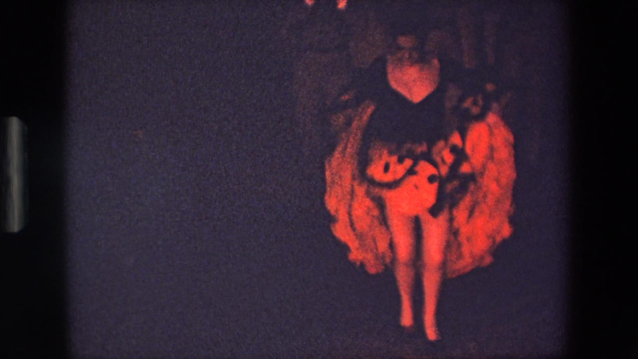 The performer faces the camera in a glowing red ruffled costume, with bare feet and a dark stage setting visible in the 8mm frame.