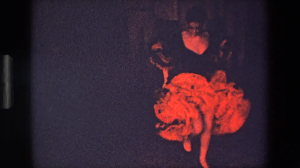 The dancer appears in motion with the red ruffled skirt spread wide, recorded from a fixed audience viewpoint in dim theatrical light.