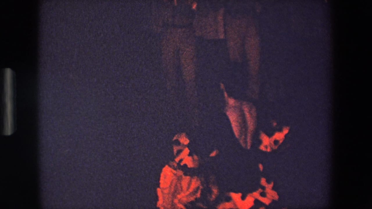 In this supplied 1967 Palermo 8mm frame, a woman in a bright red polka-dot dress dances in dim light while indistinct onlookers stand in the background.