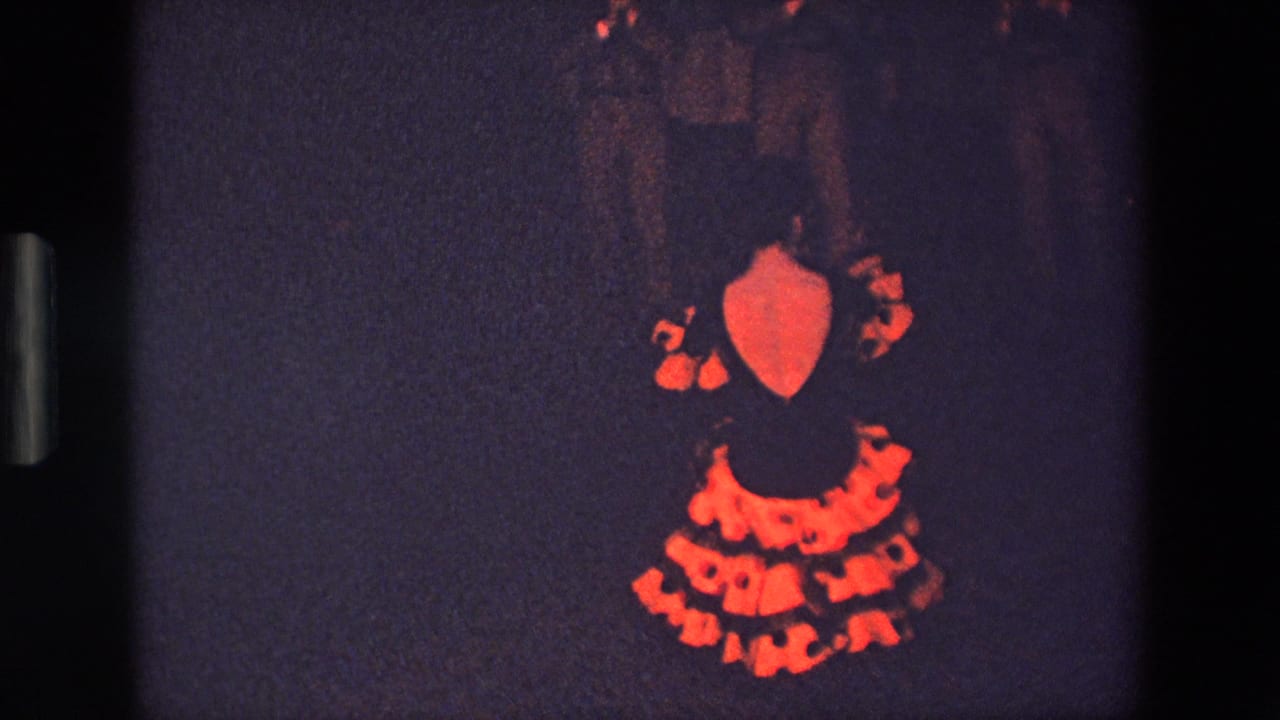 In this supplied 1967 Palermo 8mm frame, the woman faces away from the camera as her red polka-dot dress and layered skirt are visible in the dim dance space.