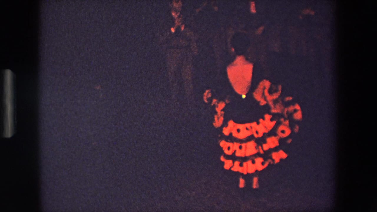 In 1967 Palermo home-movie footage, a dancer in a red-and-black ruffled dress appears under dim stage lighting with shadowed figures behind her.