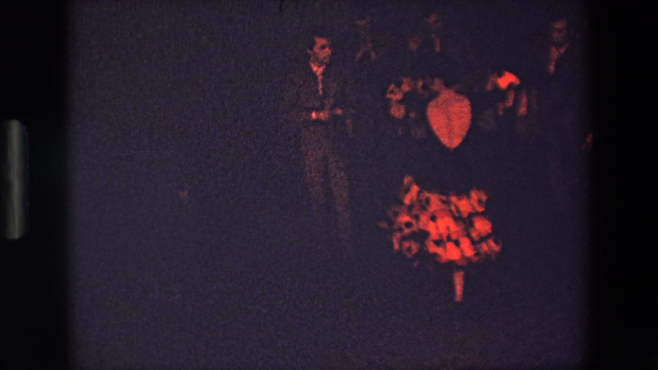 The performer appears smaller in frame, wearing a red-and-black ruffled dress on a dark stage in the 1967 Palermo home-movie clip.