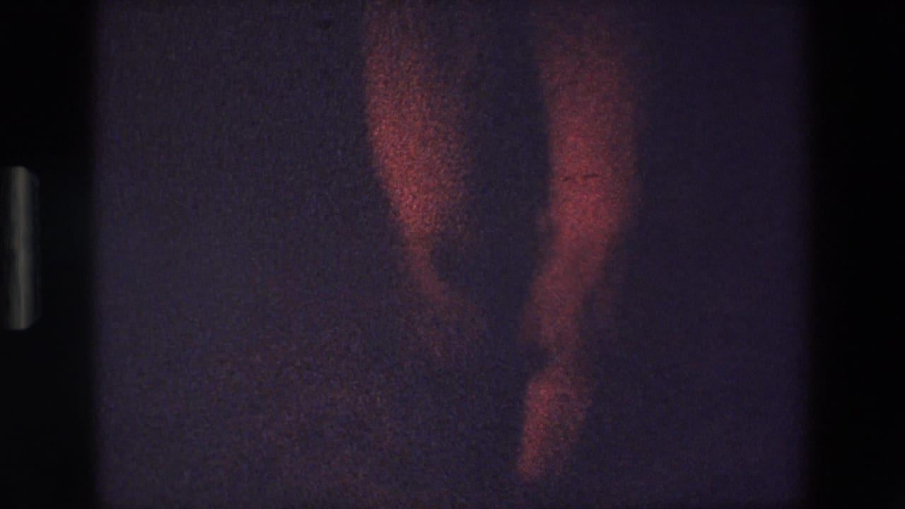 The frame emphasizes the dancer's legs and footwork beneath the red ruffled costume, with heavy grain and dim exposure from the 8mm scan.