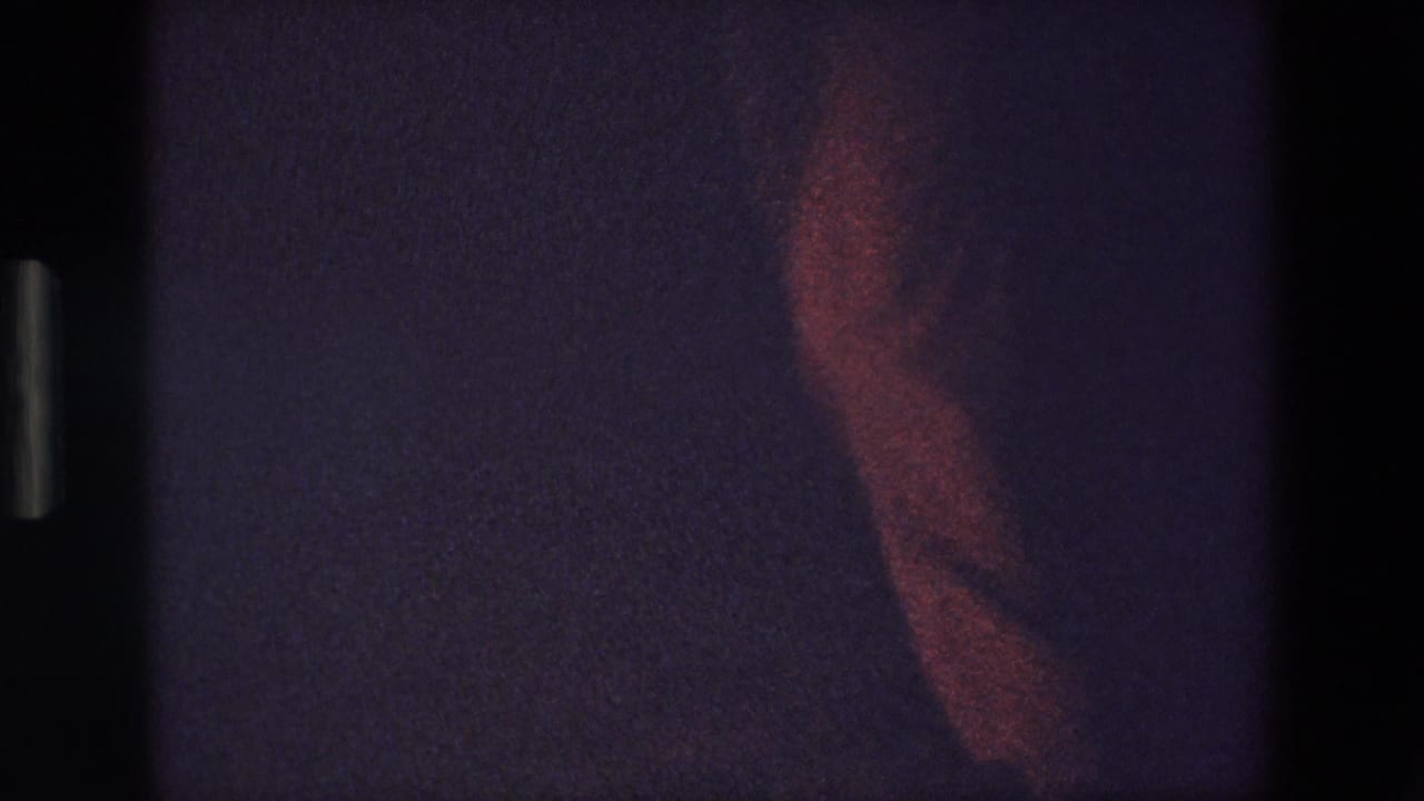 Partial red-lit figure against a dark background in low light.