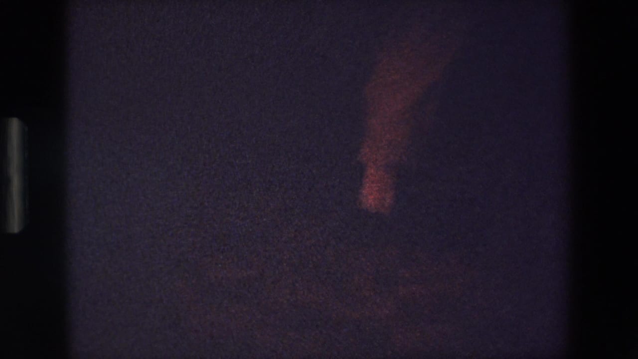 A low-light Palermo 1967 frame catches blurred lower-body movement, likely dancing feet, rendered with red tint, soft focus, and pronounced 8mm grain.