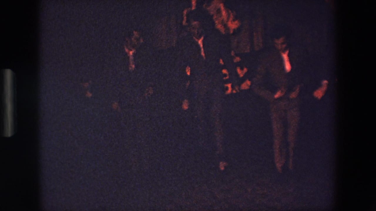 Several young men, some in jackets or ties, appear to dance or gesture together in a red-lit interior in this 1967 Palermo 8mm home-movie frame.