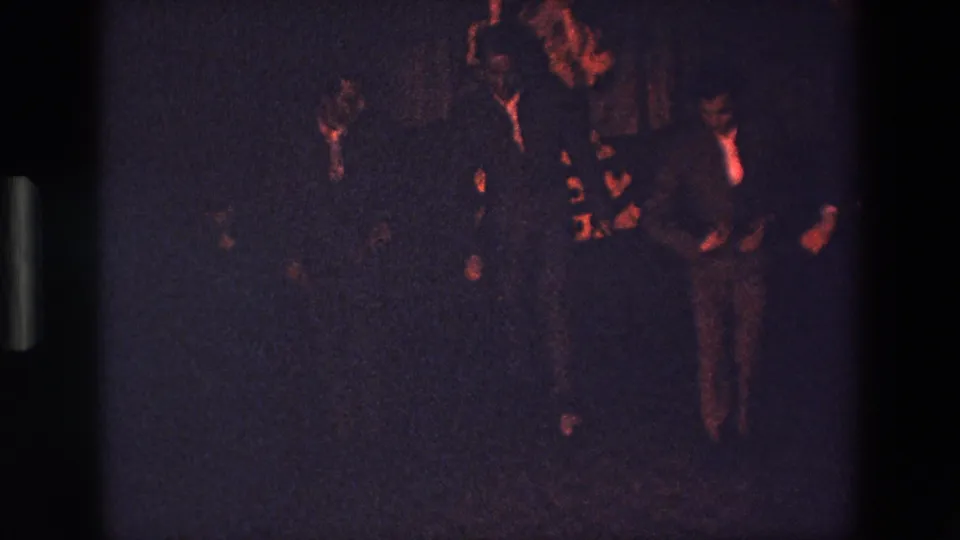 Several young men, some in jackets or ties, appear to dance or gesture together in a red-lit interior in this 1967 Palermo 8mm home-movie frame.