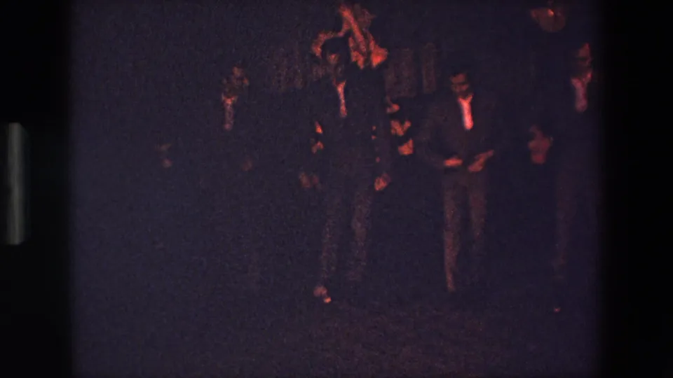 In Palermo, Italy, according to the clip metadata, several young men in suits appear to perform or dance in a dark club-like interior under warm red lighting.
