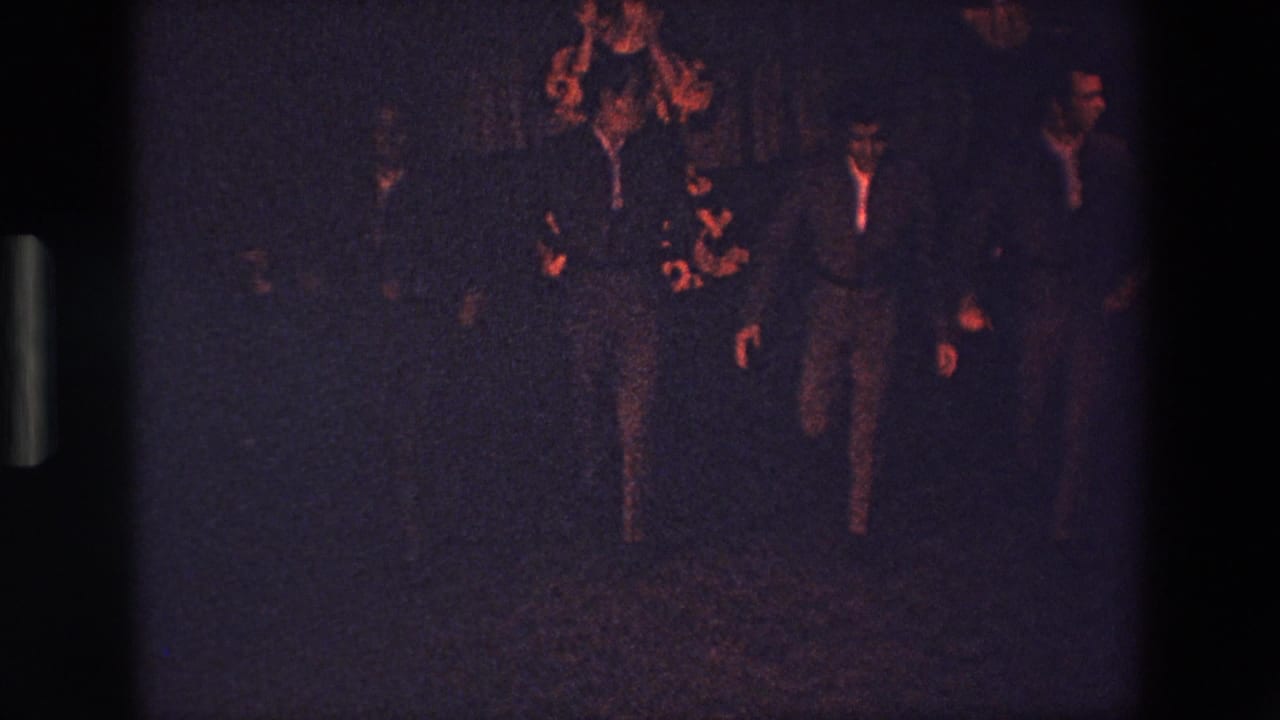 A central suited figure appears to move forward or dance while other men in suits remain nearby in the dark, warm-lit club setting.