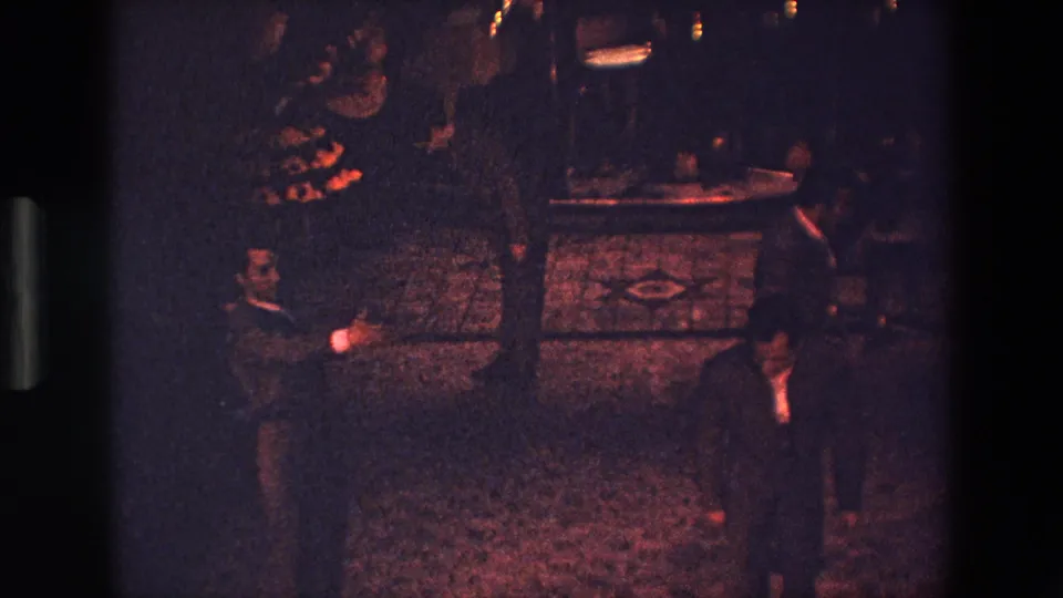 Near the end of the clip, suited men occupy the lower edge of the Palermo 1967 nighttime dance frame while other participants and faint lights remain visible in the background.