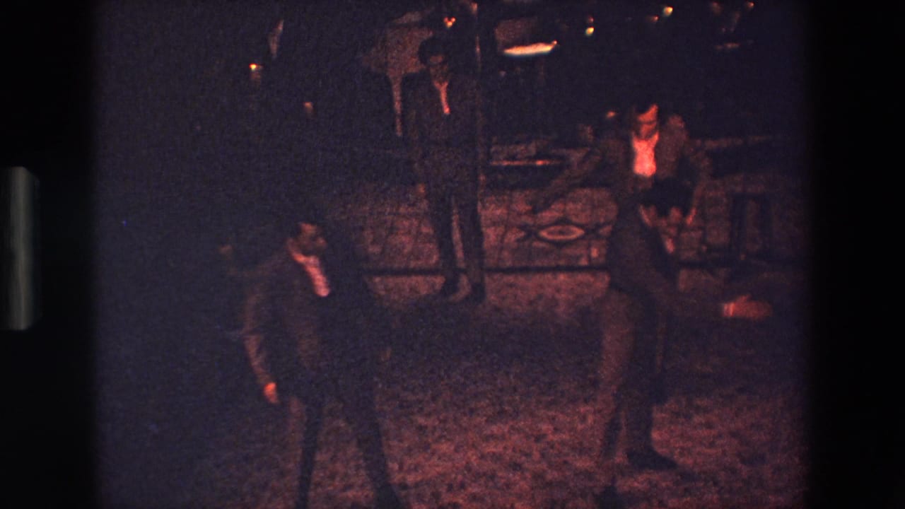 Men in dark suits appear to rehearse deliberate movements in a dim Palermo interior, with one figure bending or stepping near the foreground.