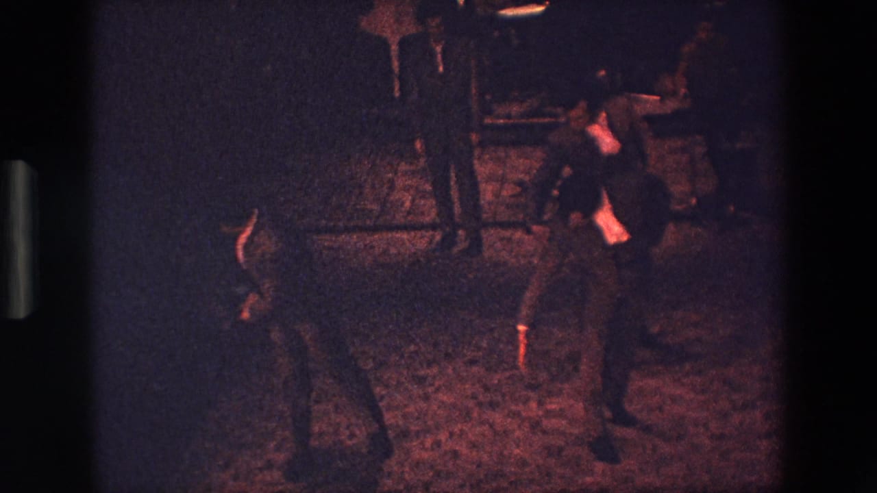 1967 Palermo 8mm frame showing performers on a dark theater stage under red-toned lighting, with details softened by low exposure and film grain.