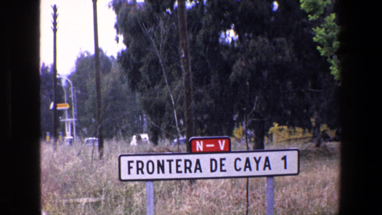 1967 Palermo-area 8mm frame showing the 'FRONTERA DE CAYA 1' roadside sign, the red 'N-V' marker, dry grass, tall trees, utility poles, and dark film edges from the home-movie scan.