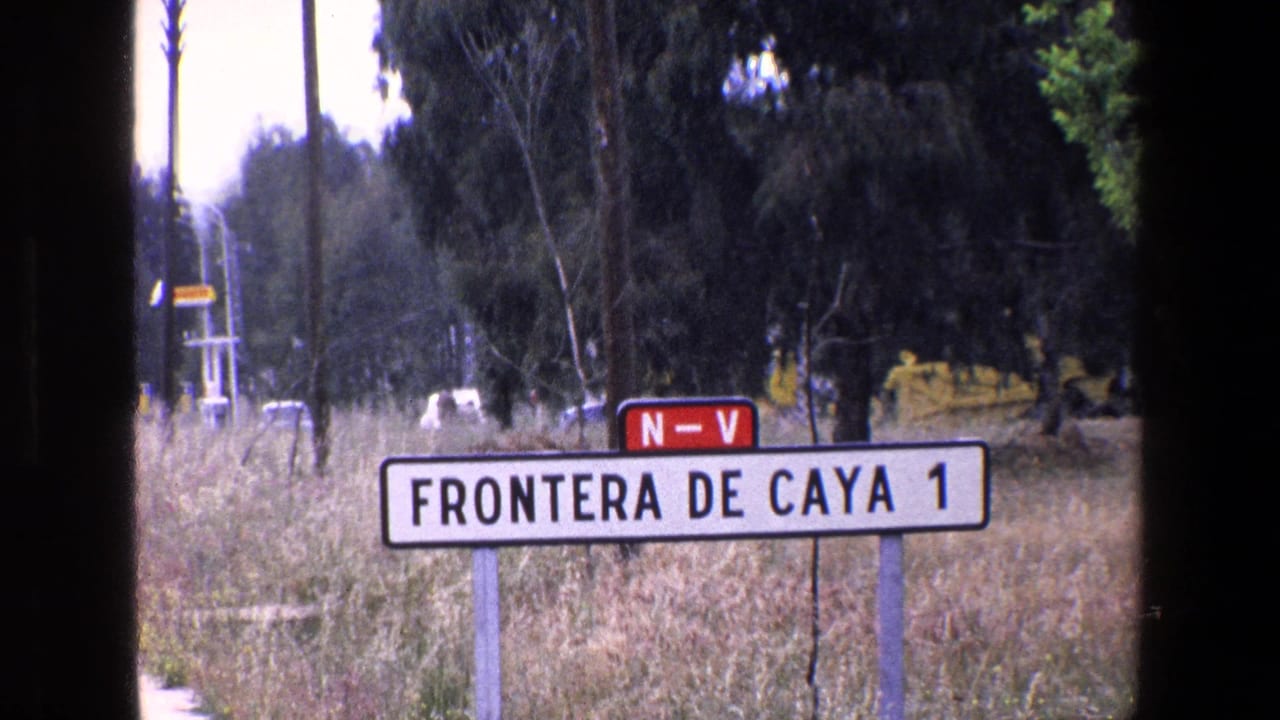 A similar 1967 8mm view of the FRONTERA DE CAYA 1 roadside sign, with dry grass, trees, and dark vertical film borders visible in the frame.