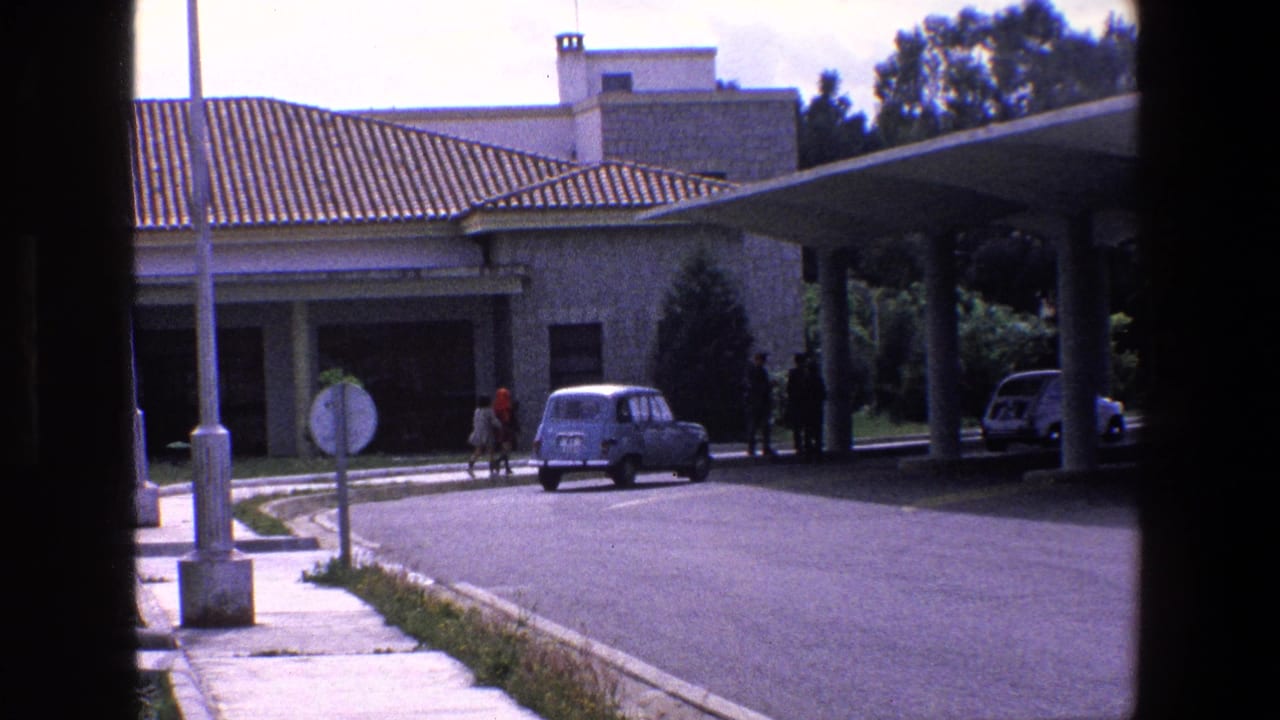 Checkpoint building with tiled roof, canopy, pedestrians, and a small vintage car.