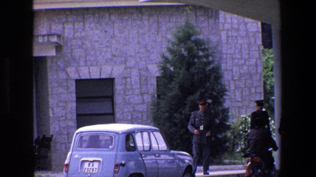 1967 Palermo exterior showing uniformed soldiers near a parked small blue car, a white stone facade, a tall tree, and the edge of a covered entrance.