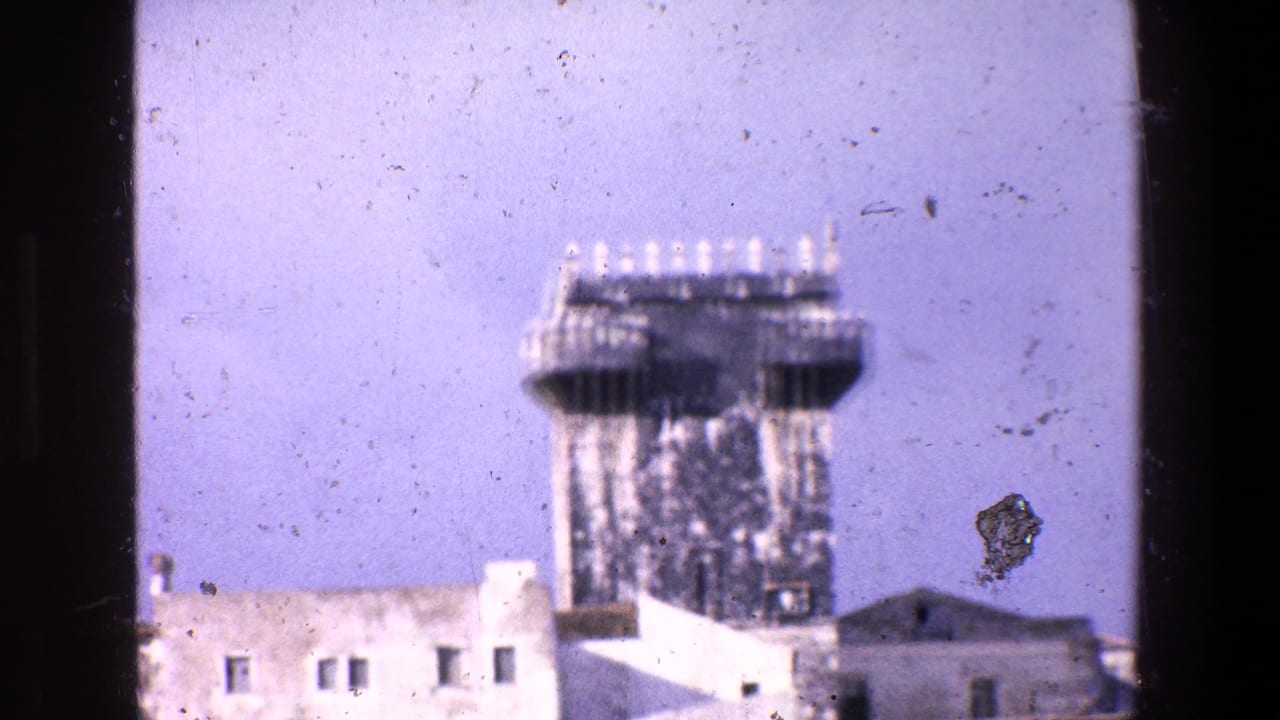 1967 Palermo home-movie frame showing a soft-focus ornate tower or architectural structure above low rooftops, with visible film dust and gate edges.