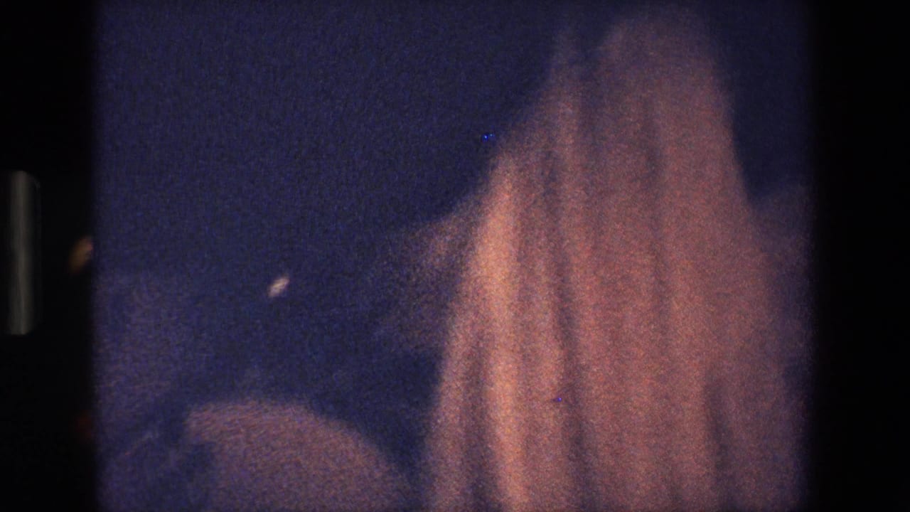 Dim 1967 Palermo frame with a robed figure or performer partially visible in low light, the pale veil or headdress blurred by motion and exposure.