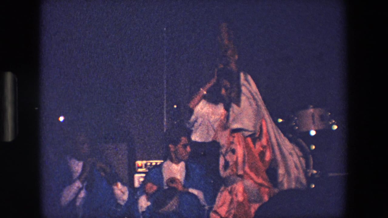 Woman in white robes and headdress dancing near spectators at night.