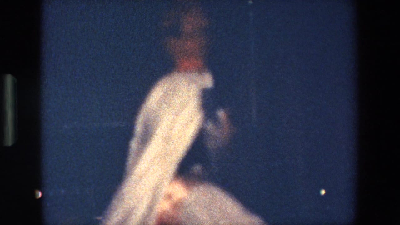 Soft-focus 1967 Palermo home-movie frame showing a dancer in a red costume and flowing white veil under dim blue stage lighting.