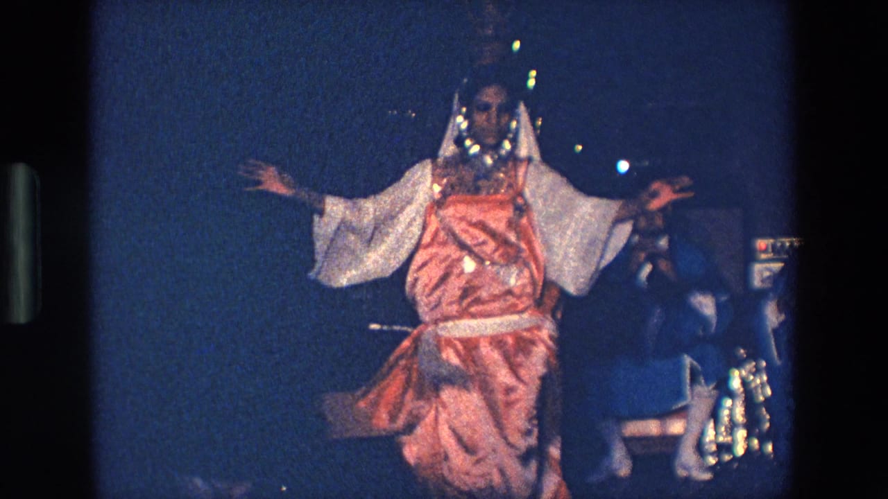 Costumed dancer faces forward with arms outstretched under blue stage light.