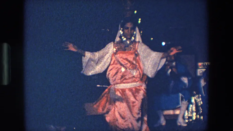 The 1967 Palermo footage shows the costumed woman facing the camera with outstretched arms against a dark blue stage background.